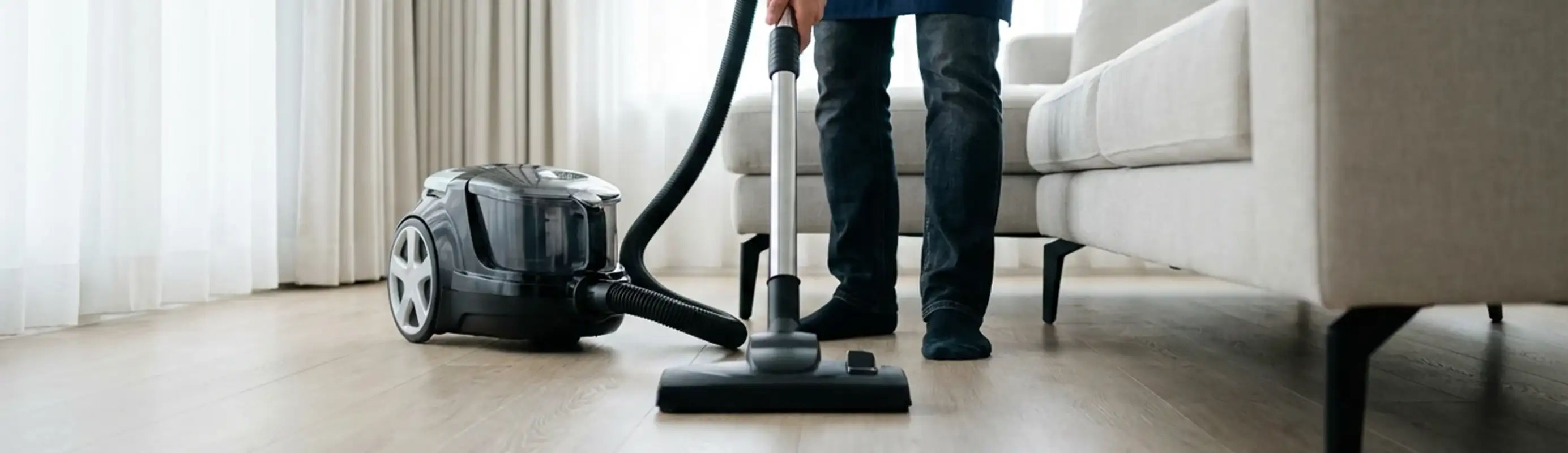 Professional house cleaner vacuuming a living room floor with a canister vacuum cleaner, Norfolk, VA.