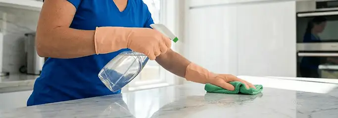 Maid service worker spraying and wiping a kitchen countertop with a microfiber cloth for sanitizing, Norfolk, VA.