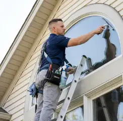Professional window cleaner on a ladder using a squeegee to clean an exterior arched window, Norfolk, VA.