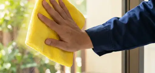 House cleaner wiping a glass window with a yellow microfiber cloth for streak-free cleaning, Norfolk, VA.